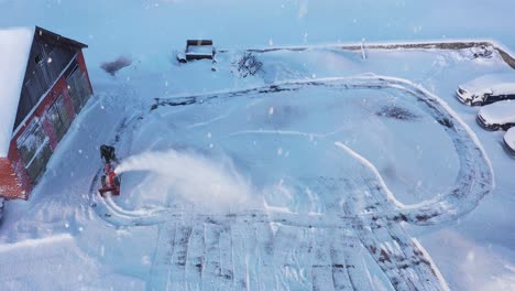 Man-blowing-snow-in-freezing-cold-during-snowfall-in-rural-landscape,-aerial-view