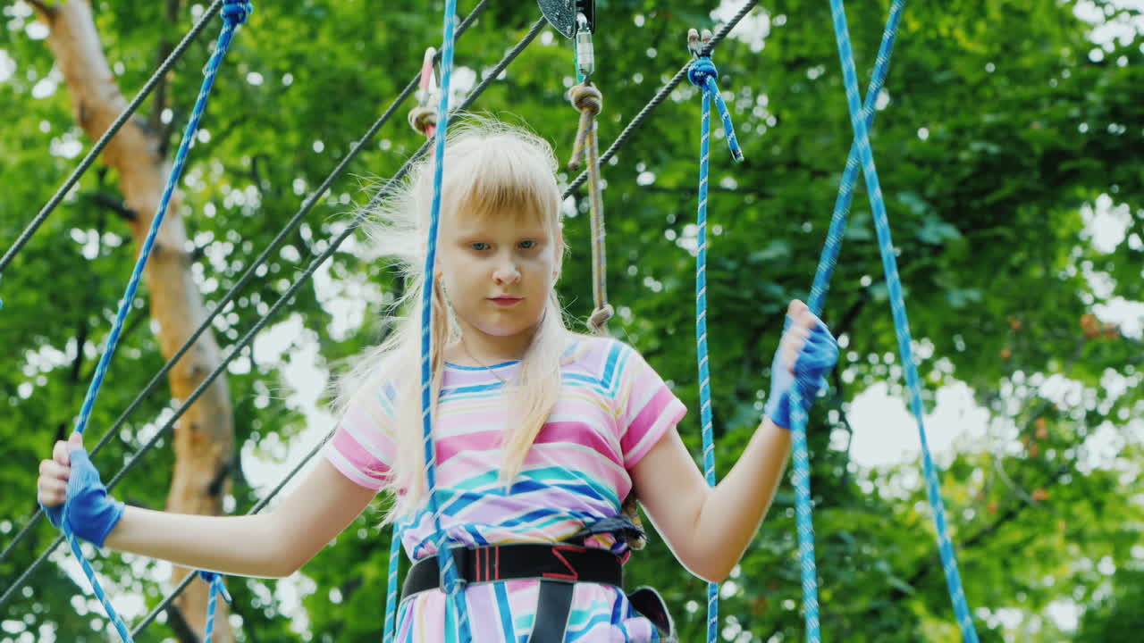 나무 사이의 밧줄을 따라 움직이는 용감한 소녀의 뒷모습은 안전 밧줄을 사용합니다