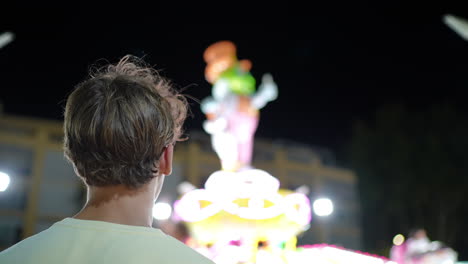 person watching brightly lit amusement park rides at night