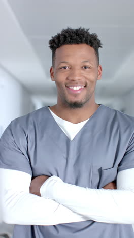 vertical video of portrait of happy african american male doctor wearing scrubs, slow motion
