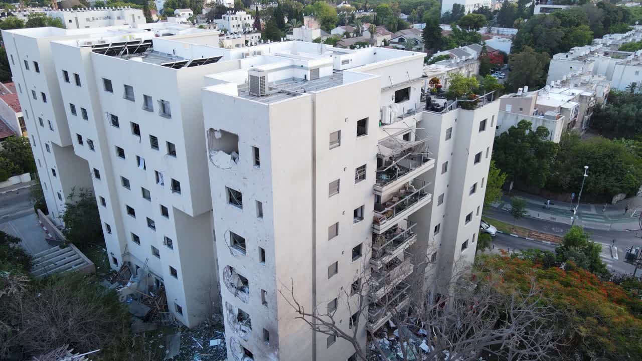 Drone approach, damaged building, missile strike, Tel Aviv, shattered windows, concrete impact, debris, balconies, urban setting, white facade, residential block