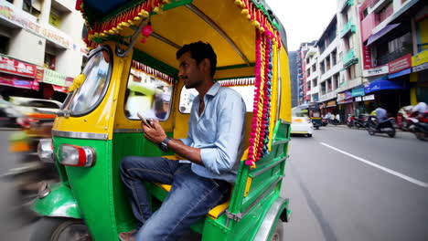 man using a mobile phone while riding in an auto-rickshaw on a city street