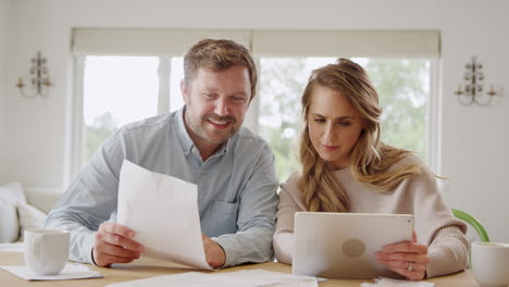 couple with digital tablet sitting at table at home reviewing domestic finances