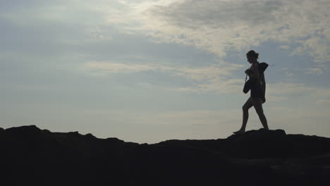 Silhouette of a woman walking on rocks against a cloudy sky
