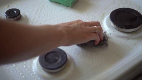 mano en un caucho verde lava una estufa moderna de vidrio-cerámica en la cocina con detergente