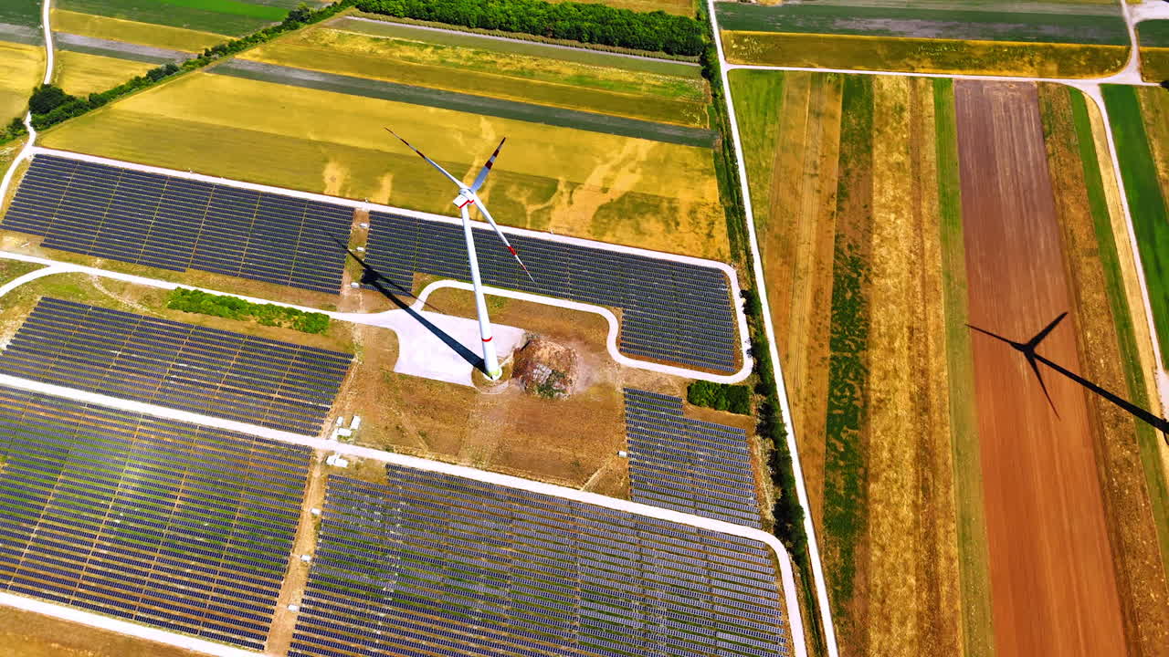 Solar and wind energy fields. This aerial view showcases solar panels and wind turbines in vibrant farmland with varied colors in the background