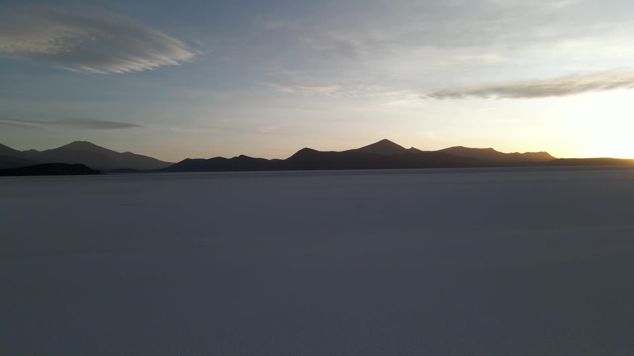 Golden hour reflection over flooded Uyuni salt flat with vehicle crossing mirror surface