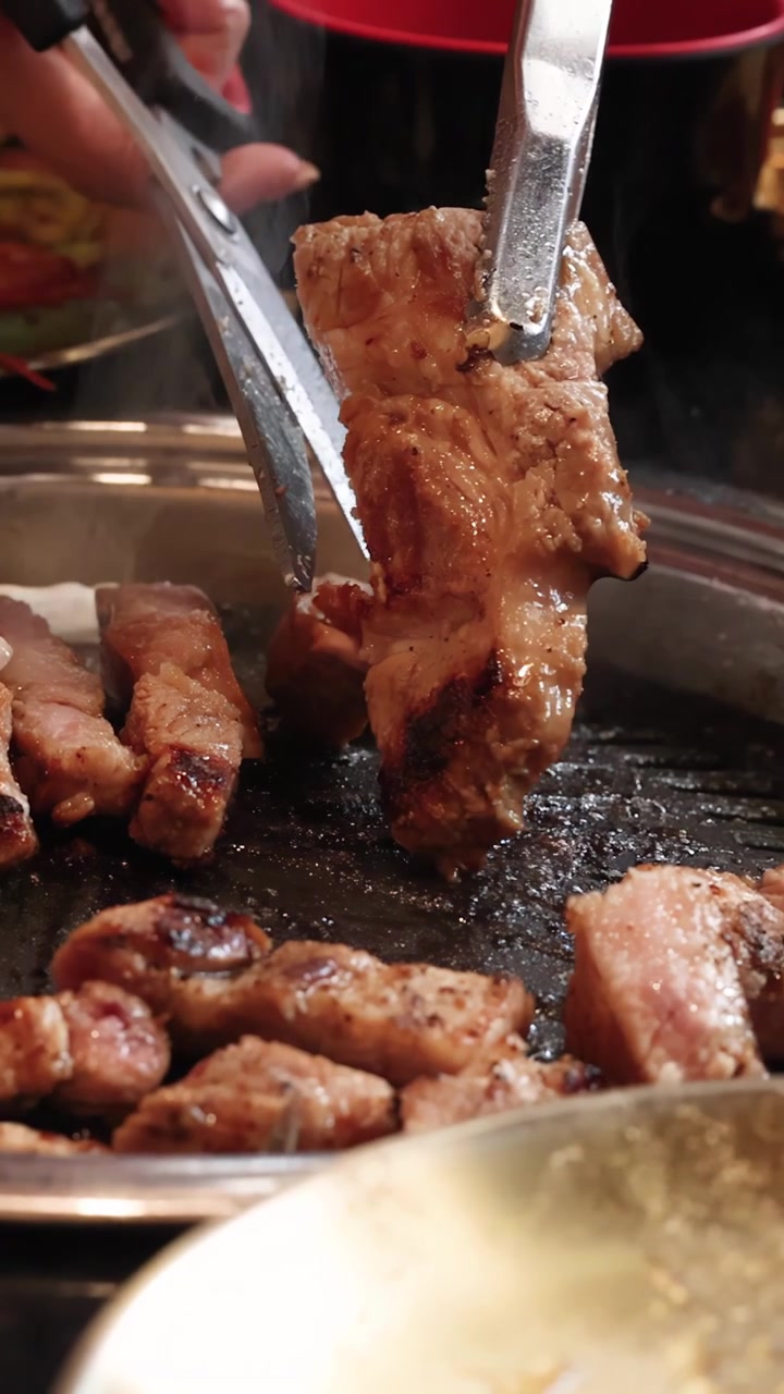 Tangan Menggunakan Penjepit untuk Memotong Perut Babi Mendesis di Atas Panggangan Barbekyu Korea Meja, Tampilan Jarak Dekat