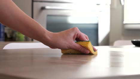 woman cleaning the kitchen table with a yellow sponge