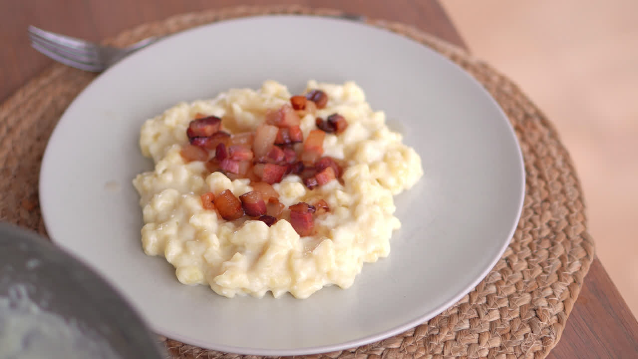 Bryndzove Halusky Dumpling In A Plate Topped With Cooked Bacon Bits, Prepared Potato Dough In A Mixing Bowl On The Side. close up, sliding rack focus