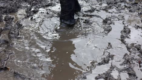 Two-young-children-messing-around-in-a-muddy-puddle,-wearing-waterproof-clothing