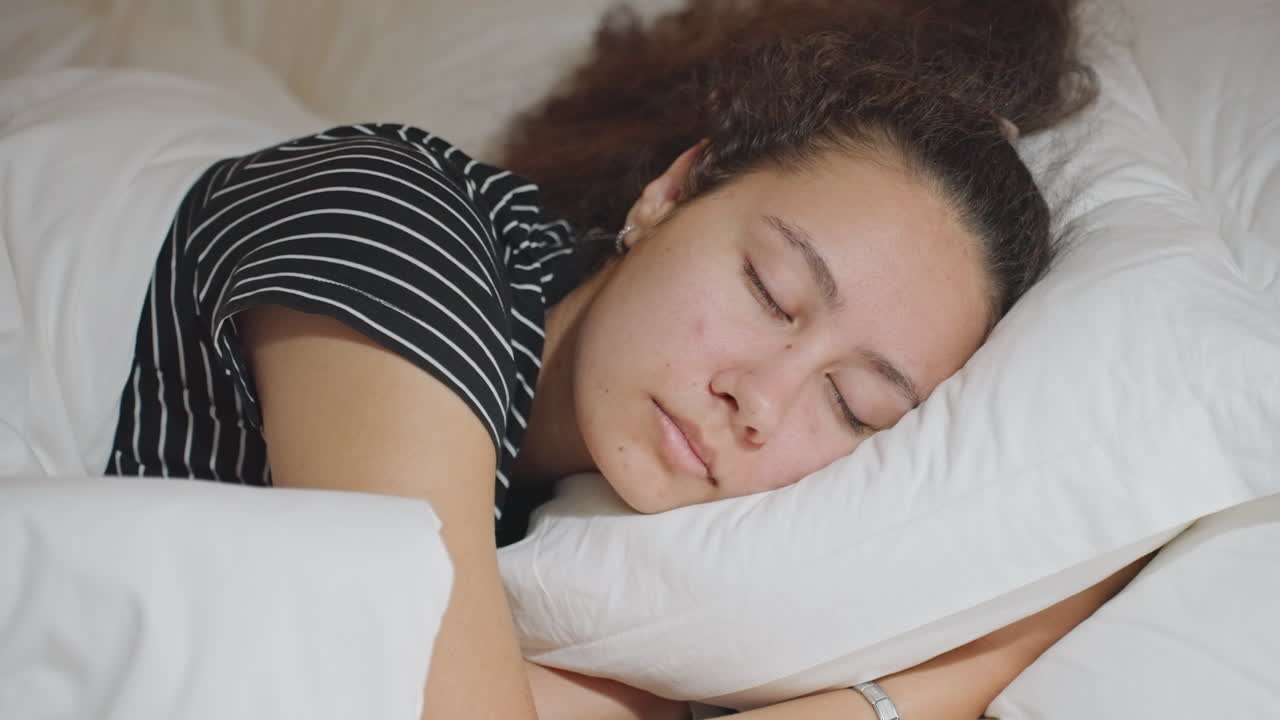 Afslappet person med blandet baggrund. En multietnisk person hviler fredeligt på et hotelværelse. En studerende med forskellige baggrunde slapper af på en pude efter en travl dag. En biracial person tager en fredfyldt lur under et roligt ophold på hotellet.