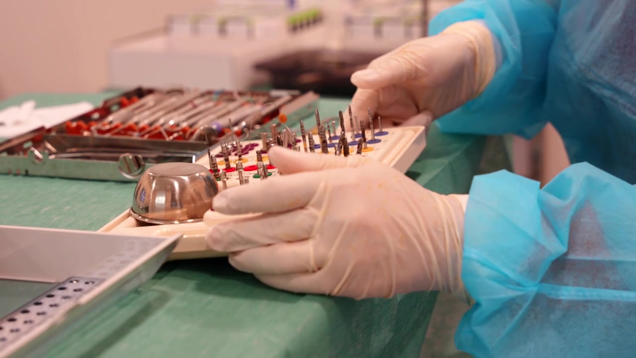 Dentist wearing gloves and PPE suit arranges small kind of tray with screwdriver heads for dental implants