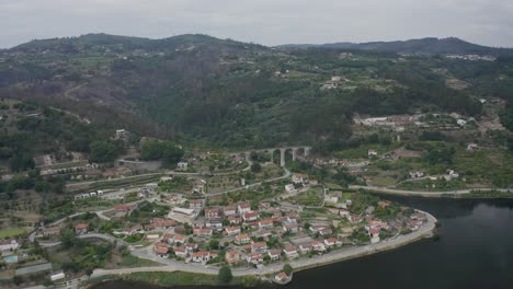 Vista-Aérea-De-Oscuras-Nubes-Tormentosas-Moviéndose-Sobre-El-Río-Douro-Y-El-Pueblo-De-Mazouco-En-El-Norte-De-Portugal