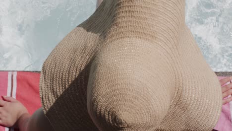 mujer biracial con sombrero de sol sentada en la piscina en cámara lenta