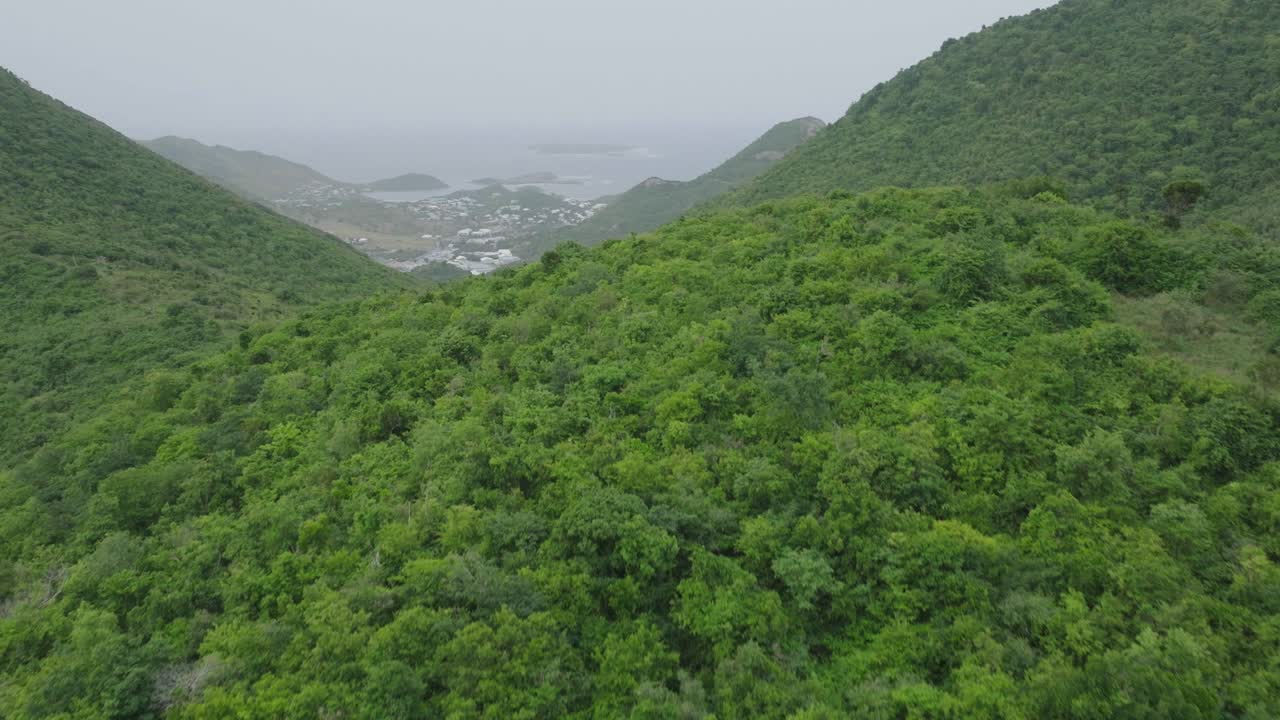 dron volando a través de las montañas llenas de vegetación de san martín durante un día nublado en la isla caribeña