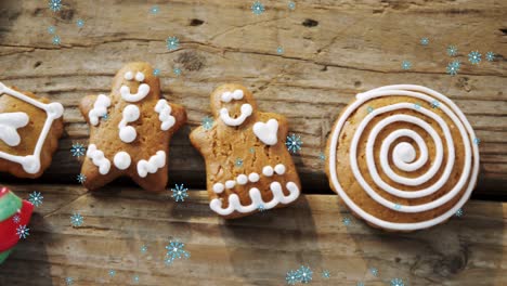 copos de nieve cayendo contra galletas de pan de jengibre hombre y caña de caramelo en la superficie de madera