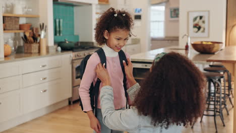 mother helping daughter with backpack in kitchen