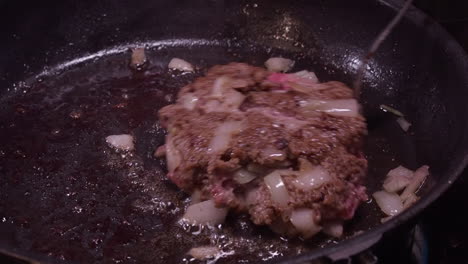 hamburguesa grasa y jugosa con cebollas movida en una sartén caliente con un tenedor