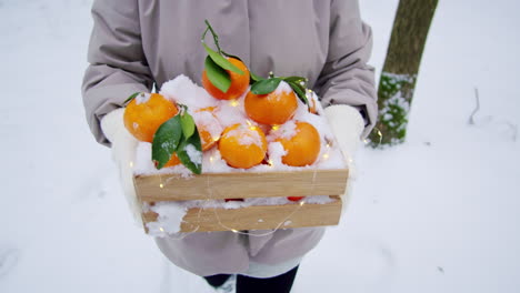 woman holding a wooden crate filled with snow-covered oranges