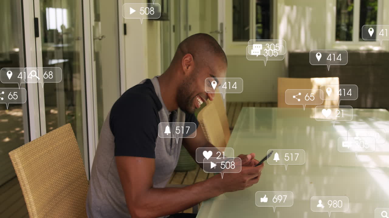 Animation of social media icons floating against african american man using smartphone at home