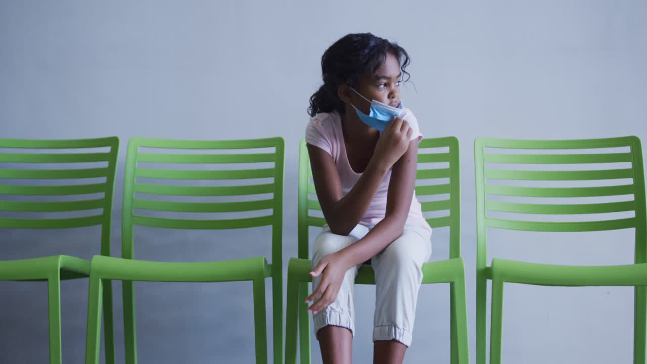 chica afroamericana bajando su máscara facial mientras estaba sentada en una silla en el hospital