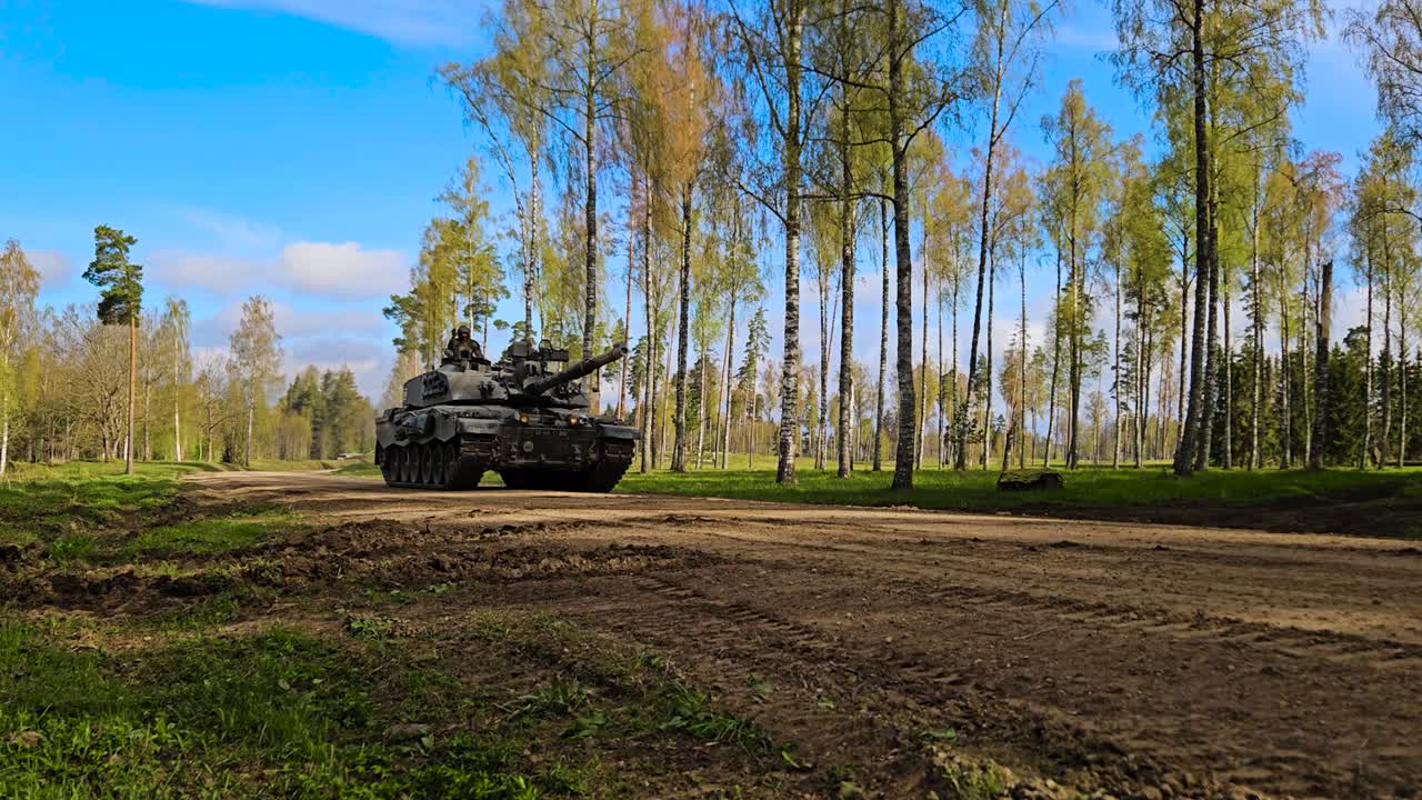 Rare beautiful video footage of a British army Challenger 2 4034 heavy armored tank driving on a dusty countryside gravel forest road during a sunny day with dust coming out from the back.