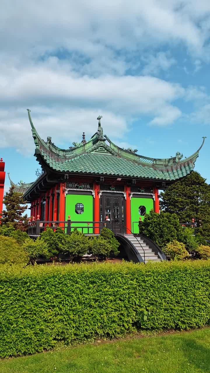 Padiglione da giardino in stile cinese con tetto verde e pilastri rossi. Struttura architettonica asiatica tradizionale con tegole ricurve e pannelli murali verde brillante.