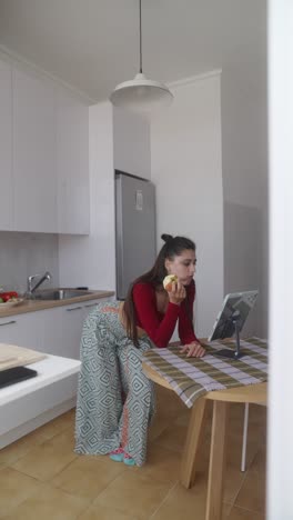 woman eating apple and using tablet in kitchen