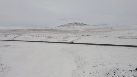 Luftaufnahme:-Panoramablick-Auf-Ein-Auto,-Das-Im-Winter-Auf-Einer-Verschneiten-Straße-In-Island-Fährt