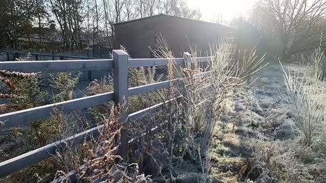 frost covered wooden fence surrounding frozen farmland barn building during golden hour