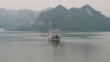 ship cruising in halong bay while other boats are anchored with misty horizon