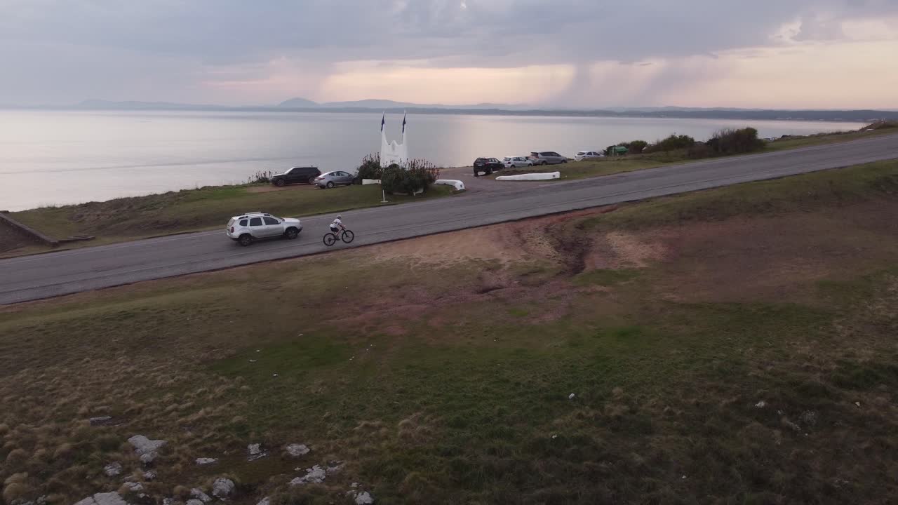 ciclista deportivo montando bicicleta de montaña en pendiente con el océano de fondo al atardecer - punta ballena, uruguay