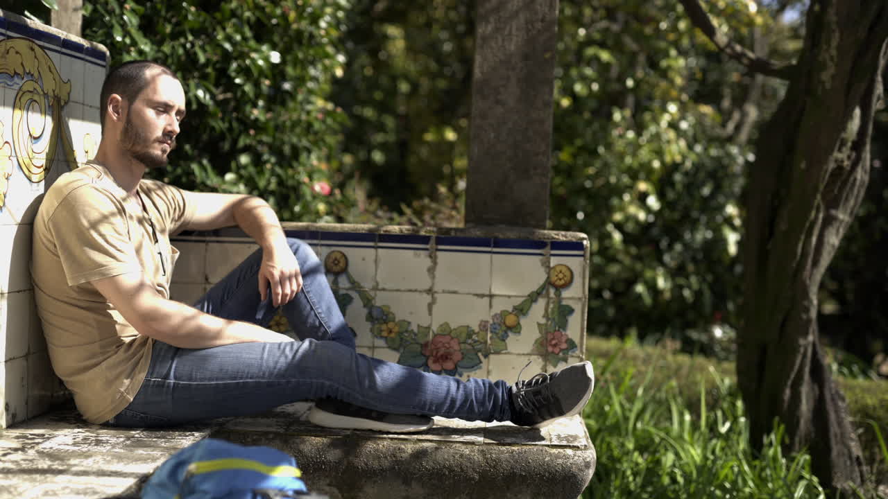 Young backpacker resting and relaxing in natural green park during sunny warm day of spring wearing trendy t-shirt