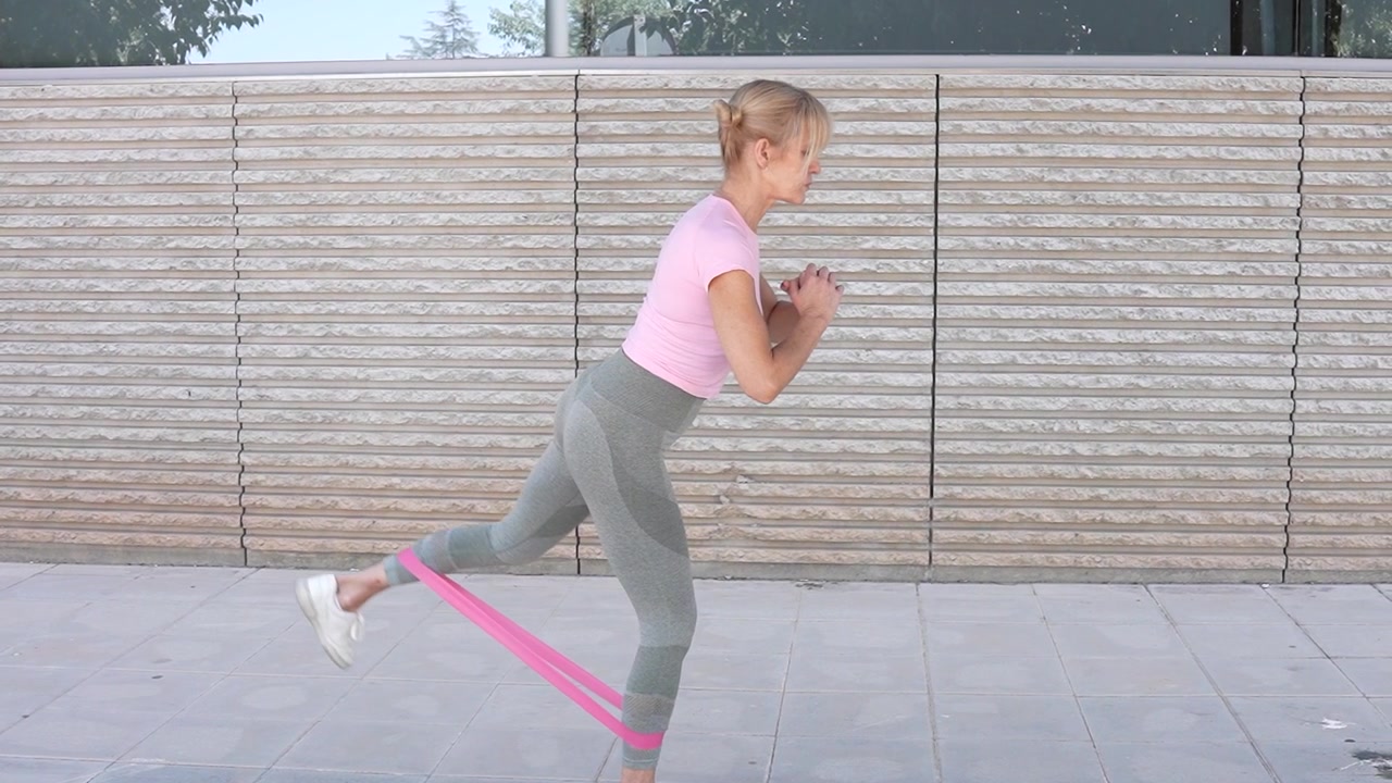 Una donna si allena all'aperto con una fascia di resistenza, indossando abbigliamento sportivo casual.