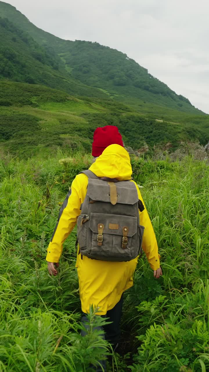 Donna con impermeabile giallo che fa escursioni tra montagne verdi e lussureggianti