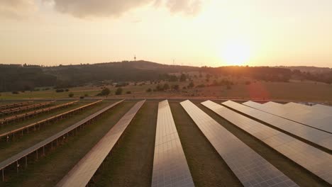 Langsame-Aufnahme-Aus-Der-Luft-Von-Einem-Solarpanelfeld-Mit-Einem-Dunstigen-Sonnenuntergang-Vom-Lauffeuer-In-Der-Vorabend-In-Hessen,-Deutschland