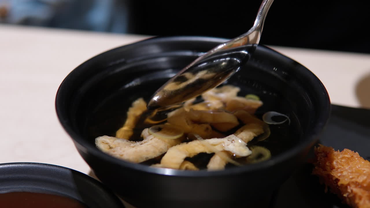 Korean cuisine, udon with sliced abura-age and green onion circles, woman's hand takes a spoon of soup