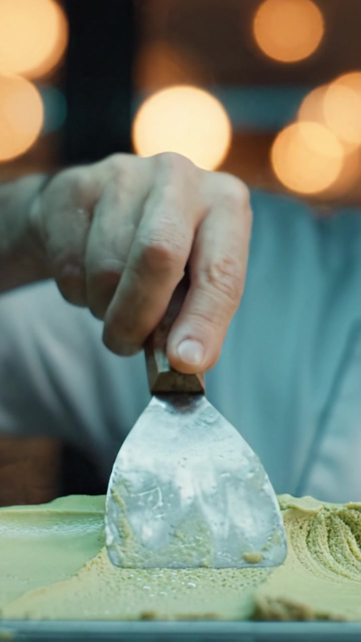 Maestro gelatiere esperto che scolpisce abilmente sapori deliziosi con strumenti di precisione in un ambiente artigianale illuminato, mettendo in mostra maestria culinaria e passione.