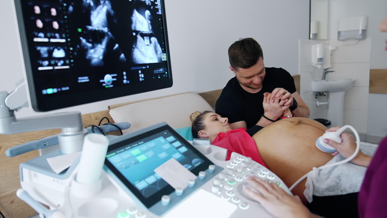 Woman on the last stages of pregnancy is checked on the ultrasonic equipment. Caring man supporting his husband.