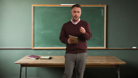 male teacher in school classroom standing in front of board teaching lesson