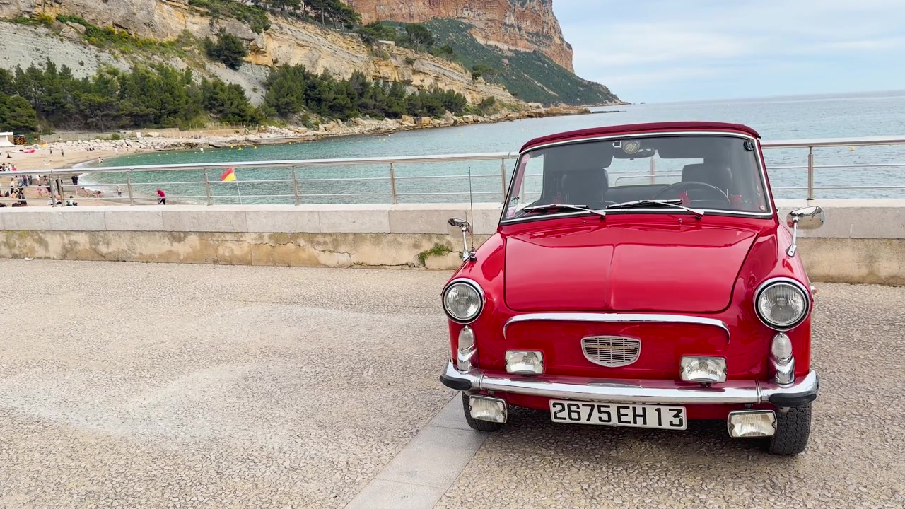 Ein klassisches rotes Cabrio steht auf einer Küstenstraße mit Blick auf das Mittelmeer geparkt.
