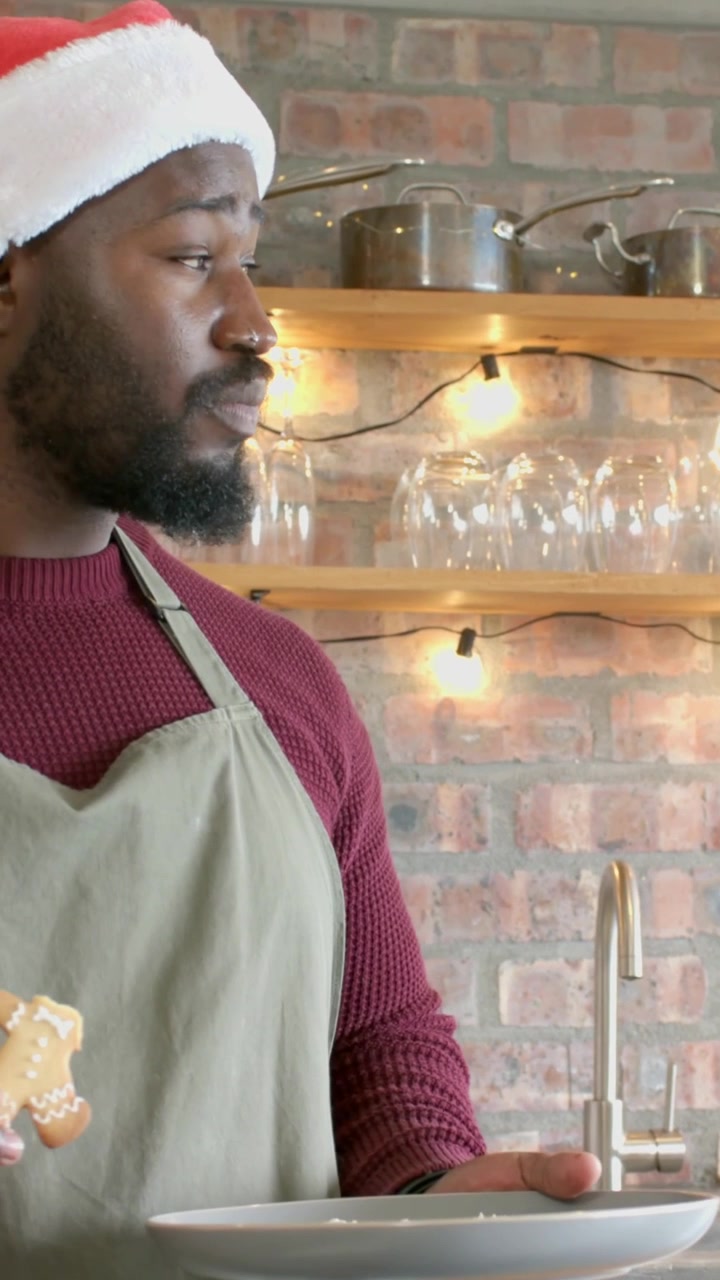 Vertical video: Eyeing plate, man in Santa hat and apron testing cookie, looking right, copy space