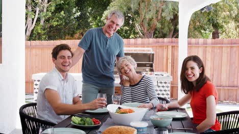 parents and adult children at table in garden look to camera