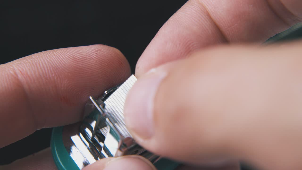 Seseorang mengeluarkan isi staples dari stapler kecil di latar belakang gelap.