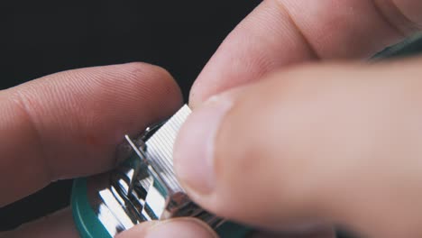 person-takes-off-clips-from-small-stapler-on-dark-background