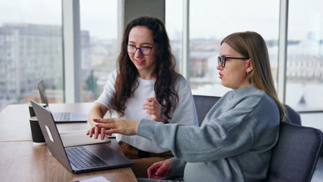 two female designers look through the photos on the laptop. positive colleagues communicate on work issues.