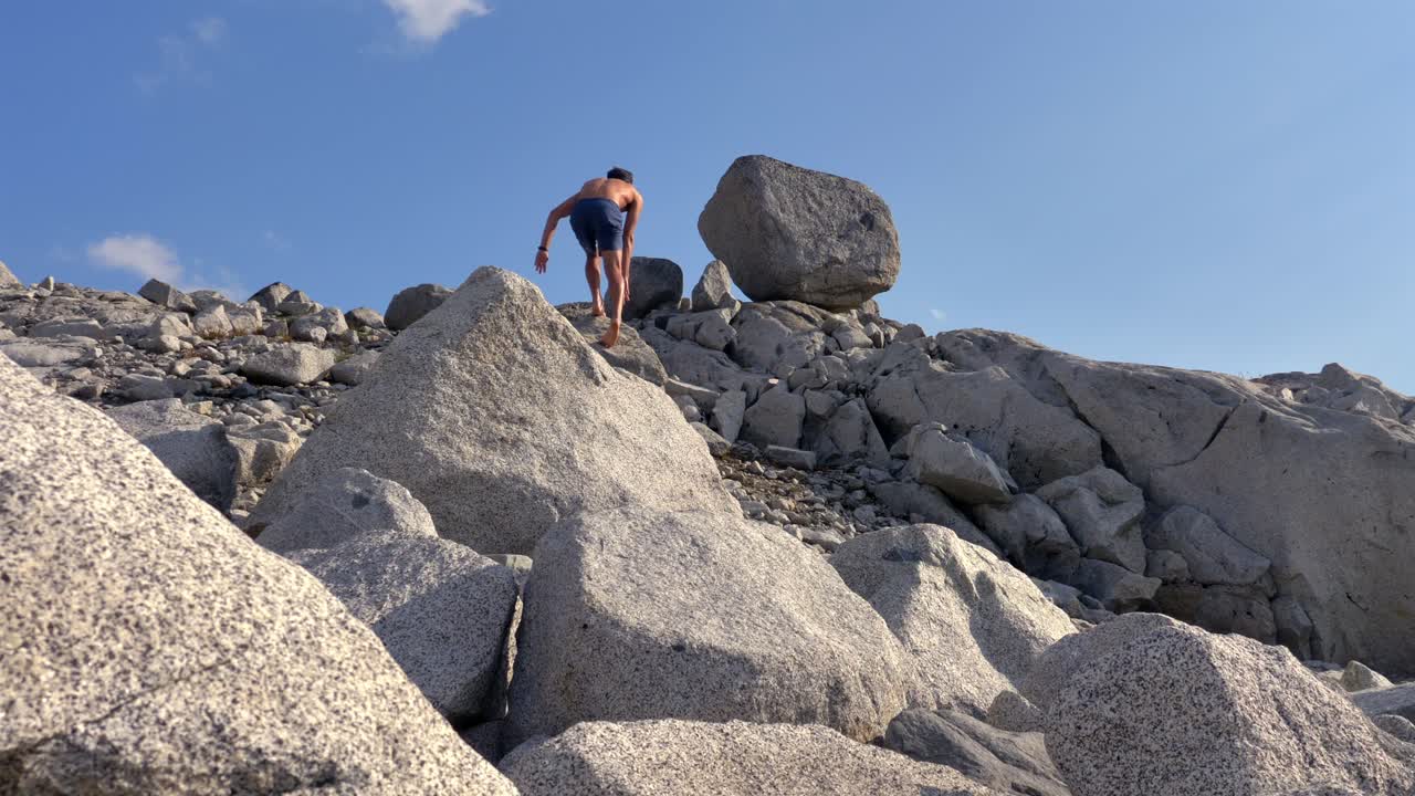 Shirtless Man Climbing Rocky Hill With Large Granite Boulders Along Wendy Thompson Hut Hike In Pemberton, BC. low angle shot