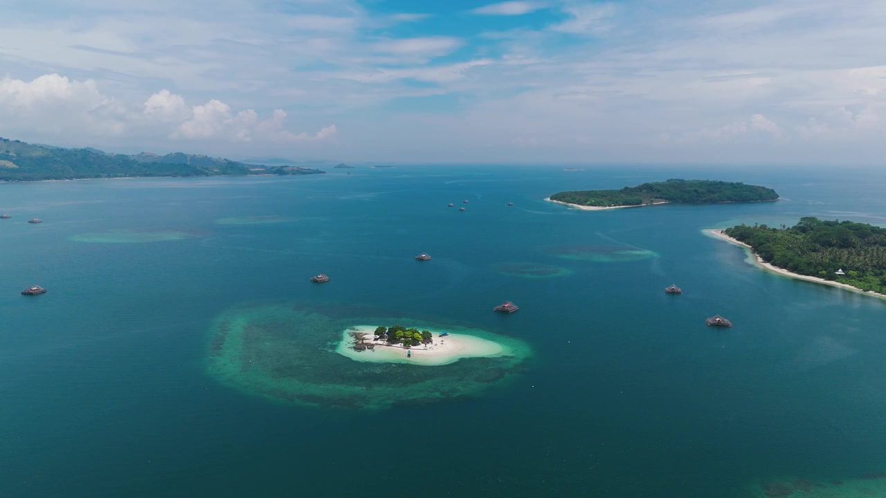 Gili Kedis, Lombok, Indonesia, menampilkan pulau tropis kecil yang dikelilingi air biru kehijauan sebening kristal, terumbu karang, dan pulau-pulau tetangga, pemandangan udara.