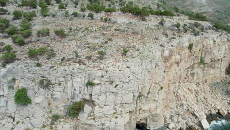 Backwards-Drone-Movement-Slowly-Revealing-A-Seaside-Cliff-With-Turquoise-Water-And-Small-Caves,-Thassos,-Greece